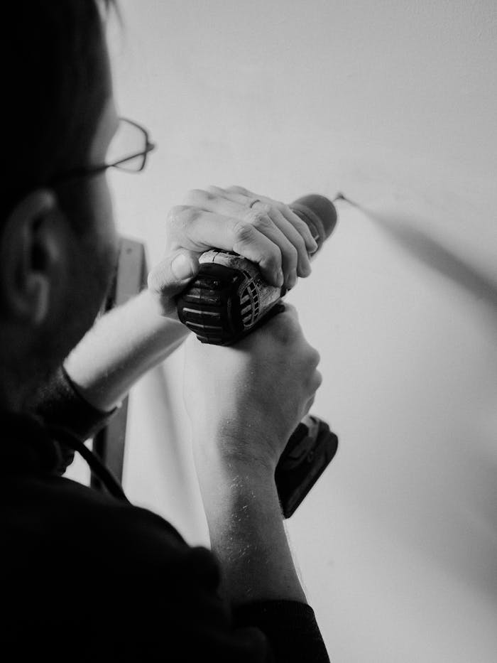 Black and white photo of a man using a drill for home improvement.